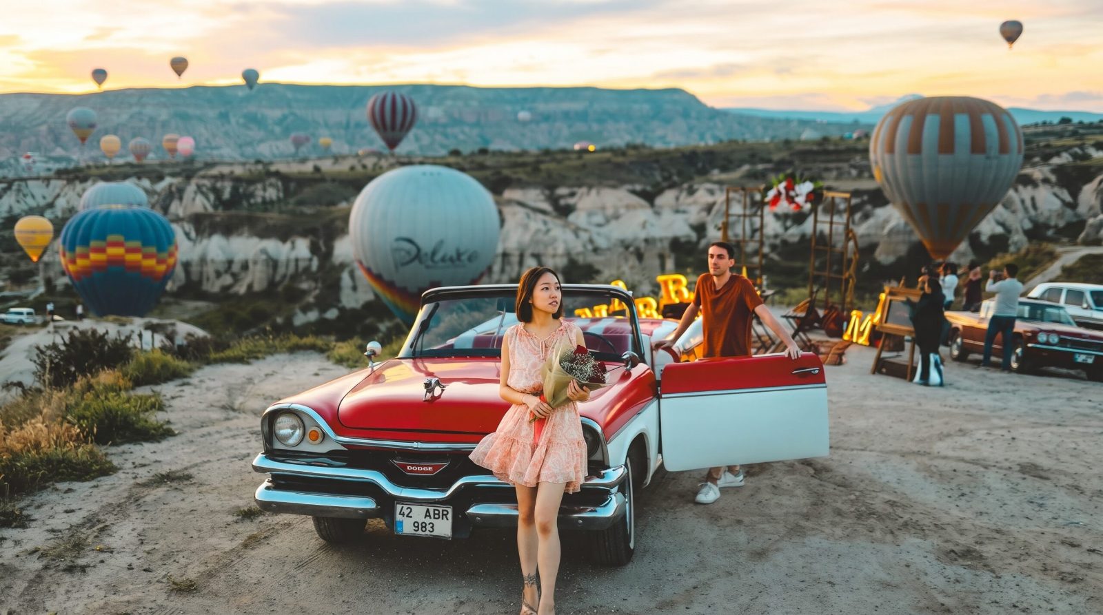 Woman with roses next to a red classic convertible at sunrise in Cappadocia